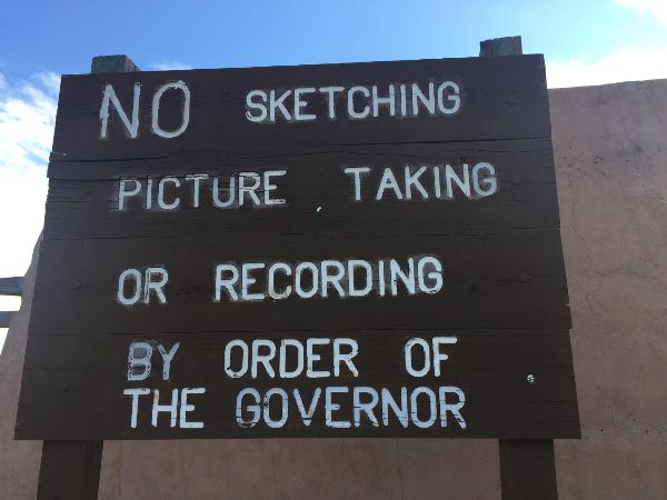 Color photo of a wooden sign in a parking lot noting, No sketching, picture taking, or recording by order of the Governor